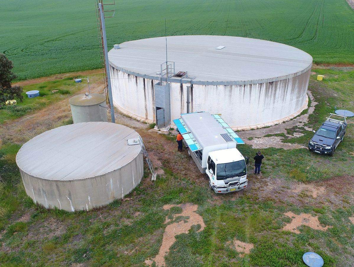 Two crew members on a tank roof holding sediment scoops