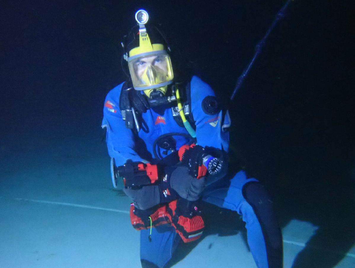 Commercial diver in a blue drysuit and full face mask mid-water inside a tank