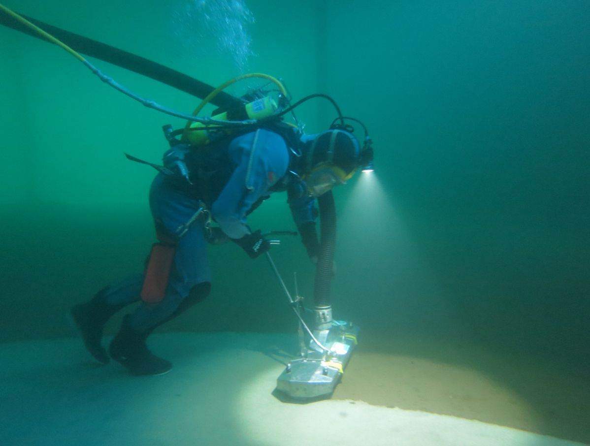Diver guiding a cleaning head across a reservoir floor in clear turquoise water
