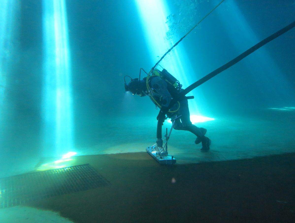 Diver descending through a reservoir under shafts of light from the open hatch