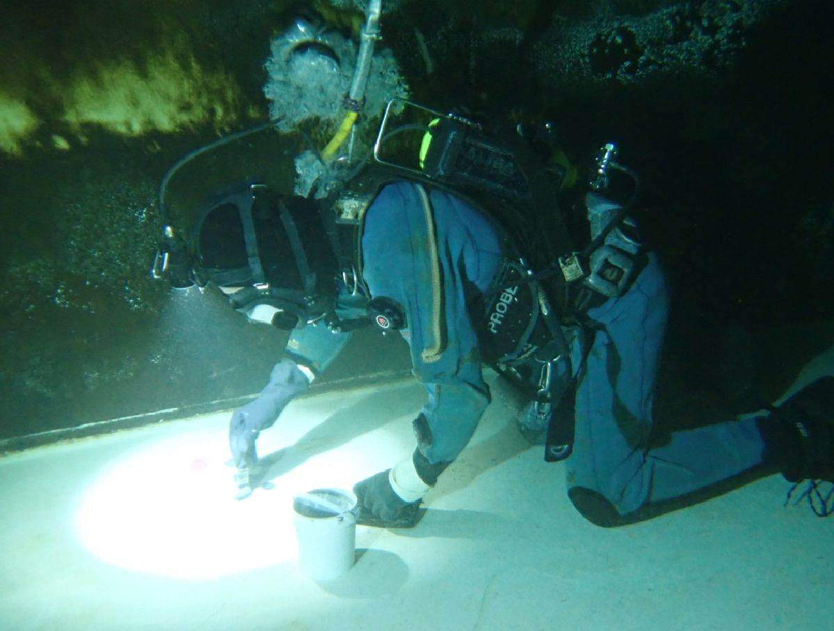 Diver working with a vacuum head on the floor of a reservoir, lit by torchlight