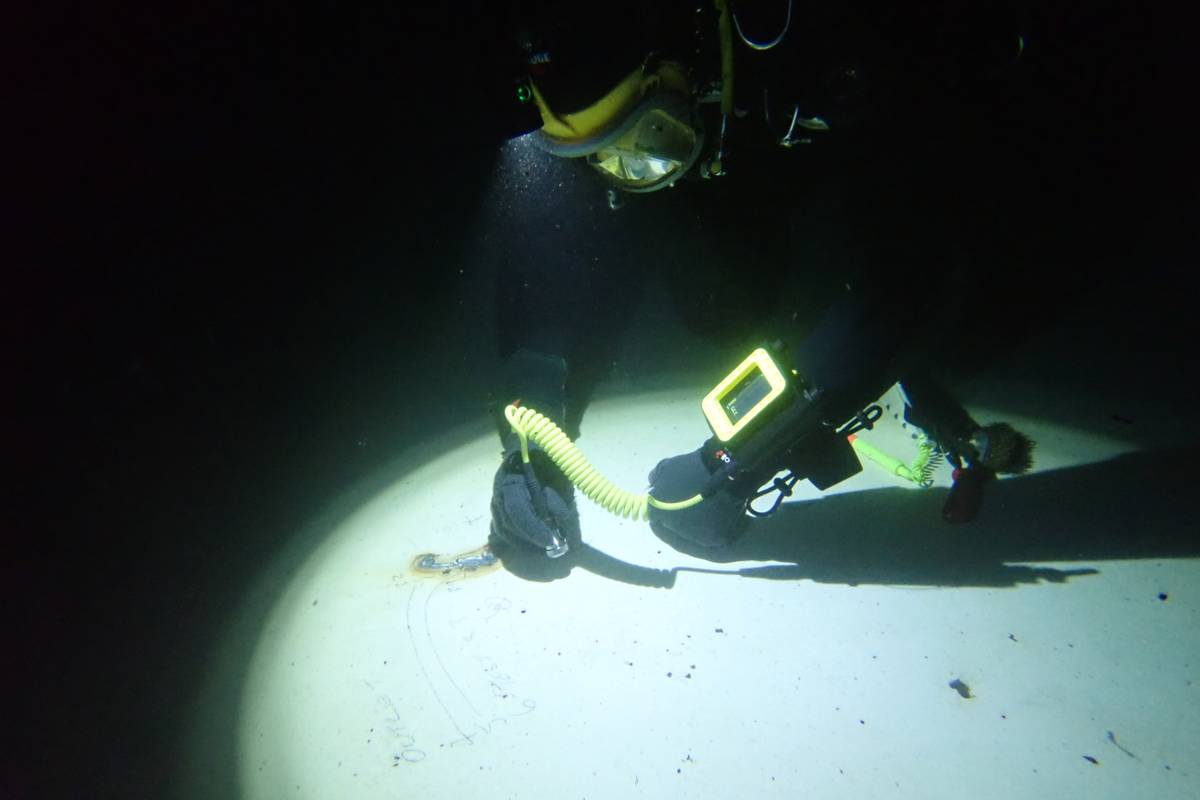 Diver taking ultrasonic thickness readings underwater with a hand-held gauge and light