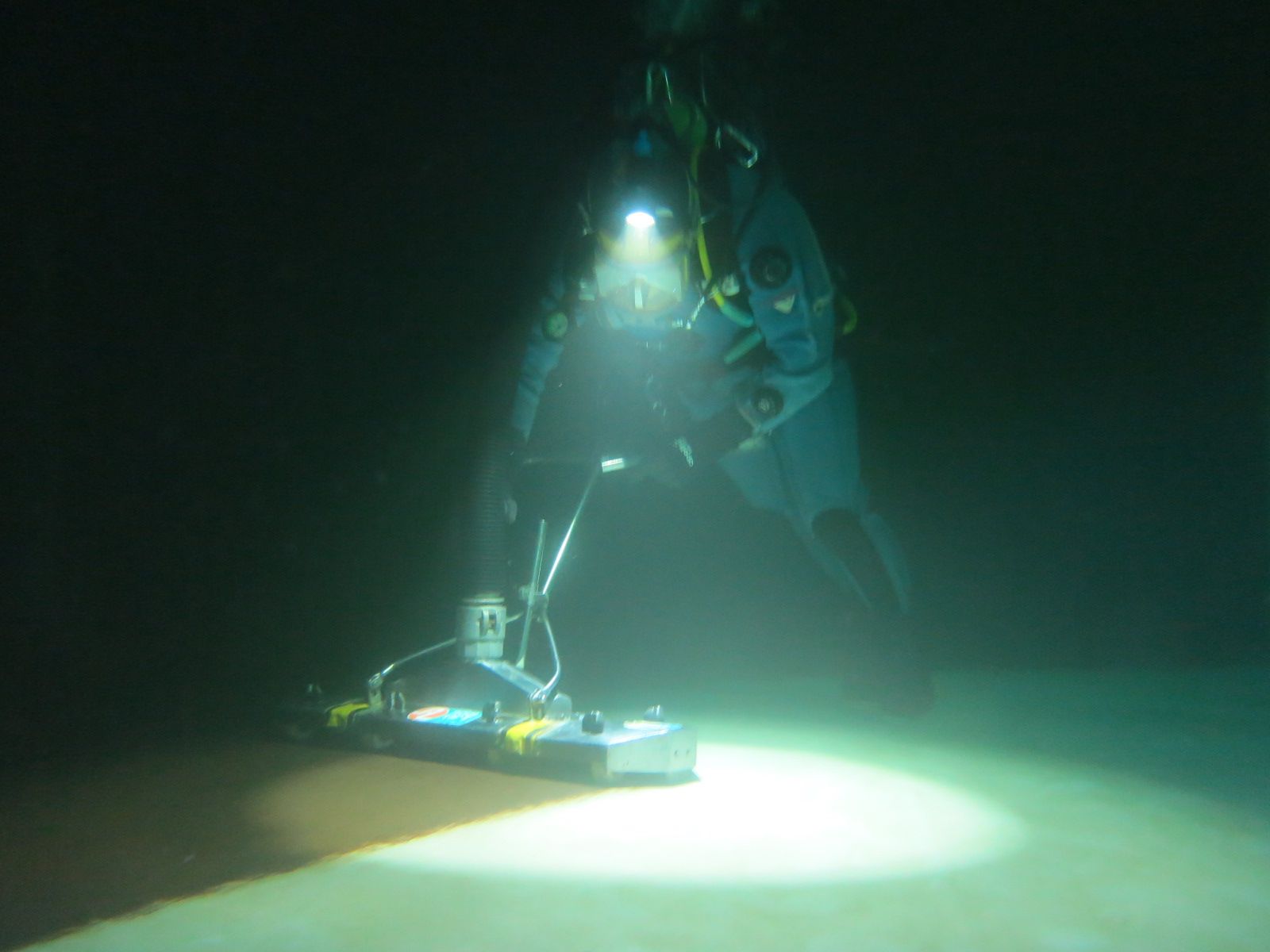 Commercial diver vacuuming sediment from the floor of a potable water reservoir by torchlight